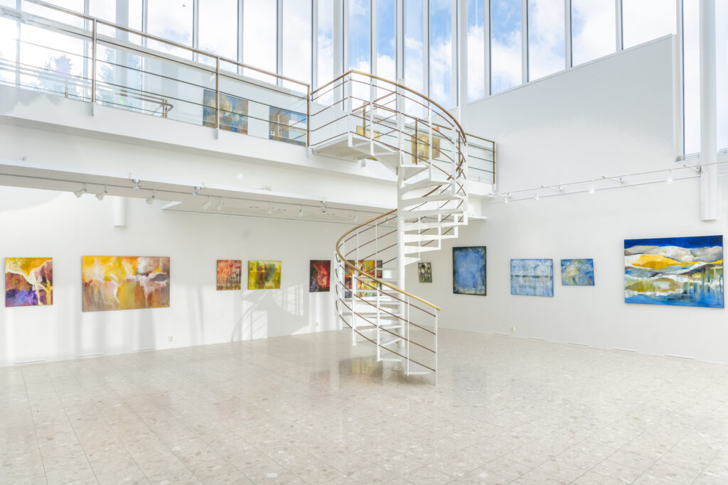 Kuvassa Kaamosgalleria, jossa seinällä värikkäitä tauluja ja kierreportaat, jotka johtavat yläparvelle.